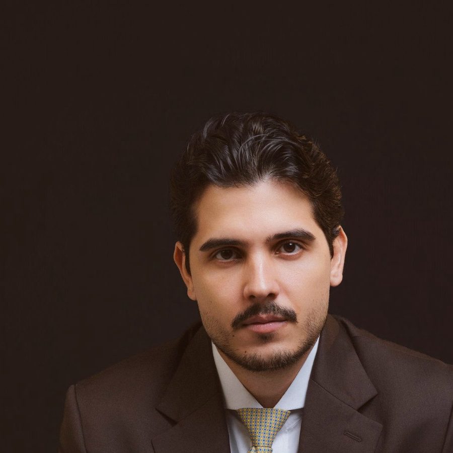 Maxwell Cruz, de terno escuro e gravata, olhando para a frente.