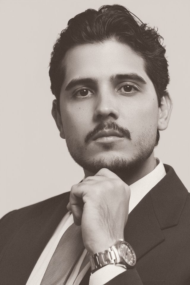 Retrato em close de Maxwell Cruz, de terno, com a mão apoiada no queixo.